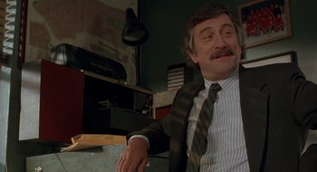 Movie still from “Cop Land” (1997), directed by James Mangold – An older man sitting in front of a desk; Medium shot, Over the shoulder angle