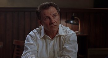 Movie still from “Cop Land” (1997), directed by James Mangold – An older man in a white shirt is sitting in front of a lamp; Close Up shot, Over the shoulder angle