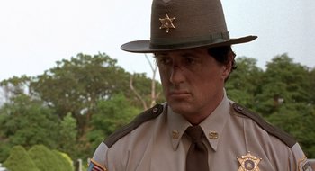 Movie still from “Cop Land” (1997), directed by James Mangold – A man in a sheriff's hat and neck tie; Close Up shot, Over the shoulder angle