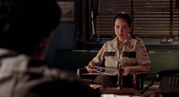 Movie still from “Cop Land” (1997), directed by James Mangold – A woman sitting in front of a man in a room; Medium shot, Over the shoulder angle