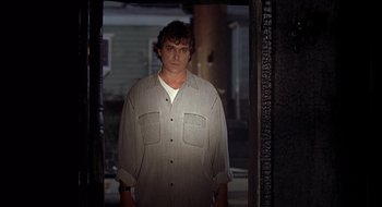 Movie still from “Cop Land” (1997), directed by James Mangold – A man standing in front of a door wearing a gray shirt; Medium shot, Low angle