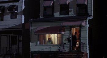 Movie still from “Cop Land” (1997), directed by James Mangold – A woman looking out of a window at a man in a doorway; Extreme Wide shot, High angle