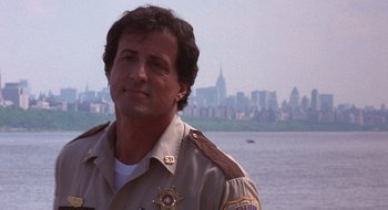 Movie still from “Cop Land” (1997), directed by James Mangold – A man in a police uniform standing in front of a body of water; Close Up shot, Over the shoulder angle