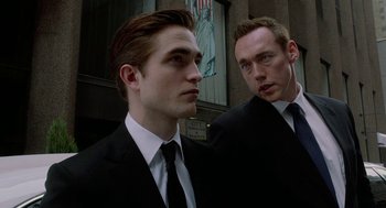 Movie still from “Cosmopolis” (2012), directed by David Cronenberg – A man in a suit and tie standing next to another man in a suit and tie; Close Up shot, Low angle