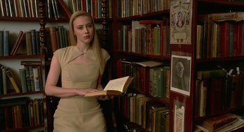 Movie still from “Cosmopolis” (2012), directed by David Cronenberg – A woman is holding an open book while standing in a library; Medium shot, Low angle