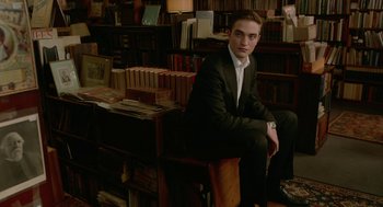 Movie still from “Cosmopolis” (2012), directed by David Cronenberg – A man in a suit sitting on a chair in a room full of books; Medium shot, High angle
