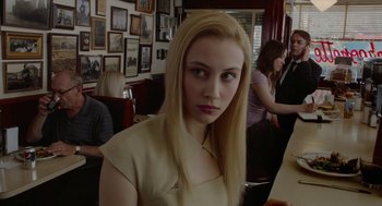 Movie still from “Cosmopolis” (2012), directed by David Cronenberg – A woman sitting at a table in front of a wall of pictures; Close Up shot, Over the shoulder angle