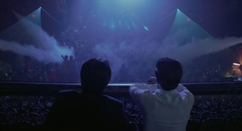 Movie still from “Cosmopolis” (2012), directed by David Cronenberg – Two people sitting in front of an audience watching a show; Medium shot, Low angle