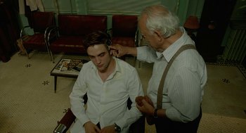 Movie still from “Cosmopolis” (2012), directed by David Cronenberg – An older man is combing a young man's hair; Medium shot, Over the shoulder angle