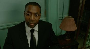 Movie still from “Cosmopolis” (2012), directed by David Cronenberg – A man wearing a suit and tie sitting in front of a lamp; Close Up shot, High angle