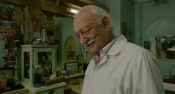 Movie still from “Cosmopolis” (2012), directed by David Cronenberg – An older man in a white lab coat in a room; Close Up shot, Over the shoulder angle