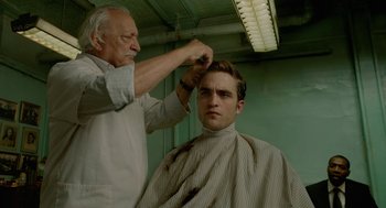Movie still from “Cosmopolis” (2012), directed by David Cronenberg – A man getting his hair cut by an old man; Medium shot, Over the shoulder angle