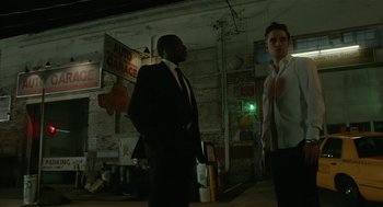 Movie still from “Cosmopolis” (2012), directed by David Cronenberg – Two men in suits standing next to each other in an alleyway at night; Medium shot, Low angle