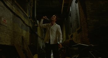 Movie still from “Cosmopolis” (2012), directed by David Cronenberg – A man standing in an alley holding a bottle of wine; Medium shot, Low angle