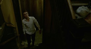 Movie still from “Cosmopolis” (2012), directed by David Cronenberg – A man in a white shirt is standing in a dark room; Wide shot, Low angle