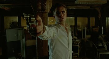Movie still from “Cosmopolis” (2012), directed by David Cronenberg – A man in a white shirt is holding a gun in his hand; Medium shot, Low angle