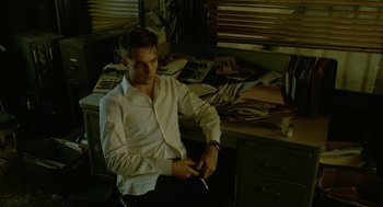 Movie still from “Cosmopolis” (2012), directed by David Cronenberg – A man sitting in front of a desk holding a pair of scissors; Medium shot, High angle