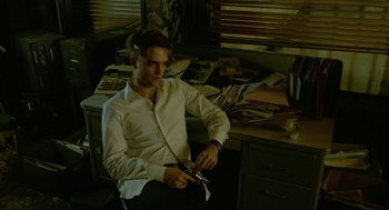 Movie still from “Cosmopolis” (2012), directed by David Cronenberg – A man sitting in front of a desk holding a pair of shears; Medium shot, High angle