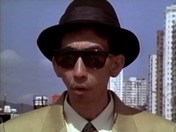 A man wearing a hat and sunglasses in front of some buildings