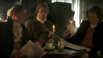 Movie still from “Crooked House” (2017), directed by Gilles Paquet-Brenner – A group of people sitting at a table with a lit candle; Medium shot, Over the shoulder angle