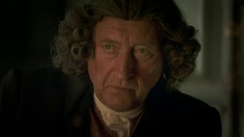 Movie still from “Crooked House” (2017), directed by Gilles Paquet-Brenner – An old man with a curly hair and a wig; Close Up shot, Over the shoulder angle
