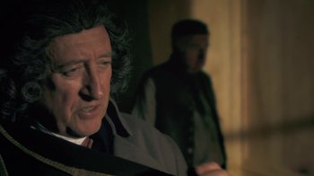 Movie still from “Crooked House” (2017), directed by Gilles Paquet-Brenner – A man in a suit and tie next to another man in a suit and tie; Close Up shot, Over the shoulder angle
