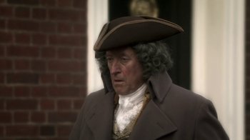 Movie still from “Crooked House” (2017), directed by Gilles Paquet-Brenner – A man in a brown coat wearing a brown hat; Close Up shot, Over the shoulder angle