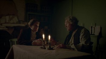 Movie still from “Crooked House” (2017), directed by Gilles Paquet-Brenner – Two people sitting at a dinner table with candles lit; Medium shot, Over the shoulder angle