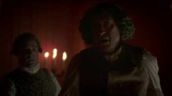 Movie still from “Crooked House” (2017), directed by Gilles Paquet-Brenner – A man in a wig and a wig stands in front of candles in a dimly - lit room; Medium shot, Over the shoulder angle