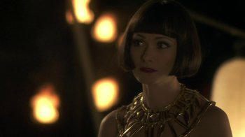 Movie still from “Crooked House” (2017), directed by Gilles Paquet-Brenner – A woman with a short haircut wearing a gold necklace; Close Up shot, Over the shoulder angle