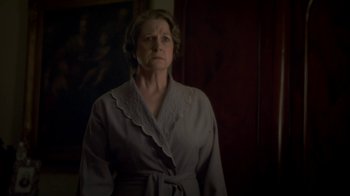 Movie still from “Crooked House” (2017), directed by Gilles Paquet-Brenner – An older woman wearing a robe standing in front of a painting; Medium shot, Low angle