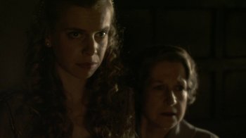Movie still from “Crooked House” (2017), directed by Gilles Paquet-Brenner – A woman and a woman standing next to each other in a dark room; Close Up shot, Over the shoulder angle