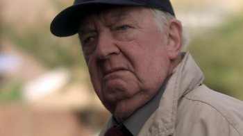 Movie still from “Crooked House” (2017), directed by Gilles Paquet-Brenner – An older man wearing a baseball cap and jacket; Close Up shot, Over the shoulder angle