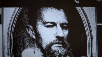 Movie still from “Crooked House” (2017), directed by Gilles Paquet-Brenner – A black - and - white photo of a man with a long beard; Extreme Close Up shot, Low angle