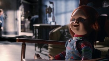 Movie still from “Curse of Chucky” (2013), directed by Don Mancini – A chucky doll sitting in a chair in a living room; Medium shot, Over the shoulder angle
