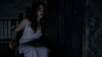 Movie still from “Curse of Chucky” (2013), directed by Don Mancini – A woman in a white dress sitting in front of a door; Medium shot, Over the shoulder angle