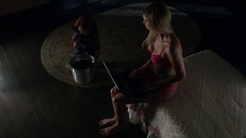 Movie still from “Curse of Chucky” (2013), directed by Don Mancini – A woman sitting on the ground with a laptop next to a doll; Wide shot, Overhead angle
