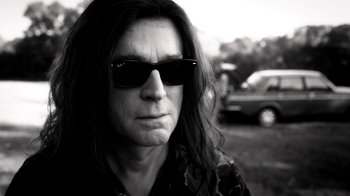 Movie still from “Curse of Chucky” (2013), directed by Don Mancini – Black and white photograph of a man with long hair wearing sunglasses; Close Up shot, Low angle