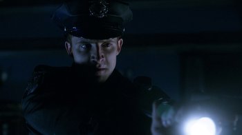 Movie still from “Curse of Chucky” (2013), directed by Don Mancini – A man in a police uniform is holding a flashlight; Close Up shot, Low angle