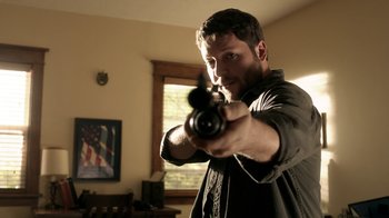 Movie still from “Curse of Chucky” (2013), directed by Don Mancini – A man holding a gun in a living room; Medium shot, Low angle