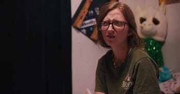 Movie still from “Cusp” (2021), directed by Isabel Bethencourt – A woman with glasses is sitting in front of a television; Close Up shot, Over the shoulder angle