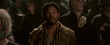 Movie still from “Cyrano” (2021), directed by Joe Wright – A man in a brown jacket is looking at the camera; Close Up shot, Over the shoulder angle
