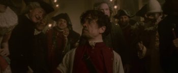 Movie still from “Cyrano” (2021), directed by Joe Wright – A group of people standing in a room with lights; Medium shot, Over the shoulder angle