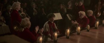 Movie still from “Cyrano” (2021), directed by Joe Wright – A group of people sitting at a table with candles; Medium shot, Over the shoulder angle