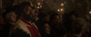 Movie still from “Cyrano” (2021), directed by Joe Wright – A group of people sitting in a dark room; Close Up shot, Over the shoulder angle