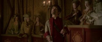Movie still from “Cyrano” (2021), directed by Joe Wright – A man standing in front of a woman in front of a chandelier; Medium shot, Low angle