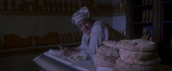 Movie still from “Cyrano” (2021), directed by Joe Wright – A man sitting in front of a table of food; Medium shot, High angle