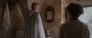 Movie still from “Cyrano” (2021), directed by Joe Wright – A woman standing in front of a mirror in a room; Medium shot, Over the shoulder angle