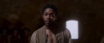 Movie still from “Cyrano” (2021), directed by Joe Wright – A man in a brown shirt is looking at the camera; Close Up shot, Over the shoulder angle