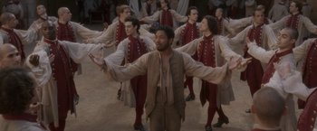 Movie still from “Cyrano” (2021), directed by Joe Wright – A group of men in medieval garb dancing in a circle; Wide shot, High angle